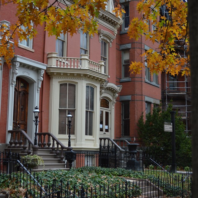 A rowhouse with a brick sidewalk and autumn leaves in front of it
