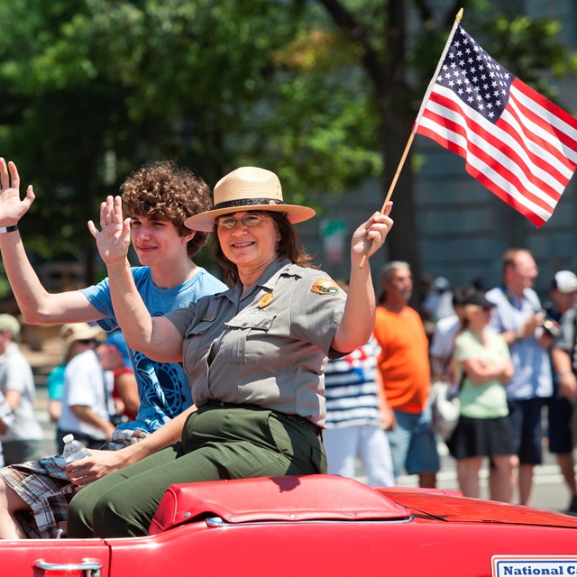 A Park Ranger waves an American Flag from a parade car in the Independence Day Parade.