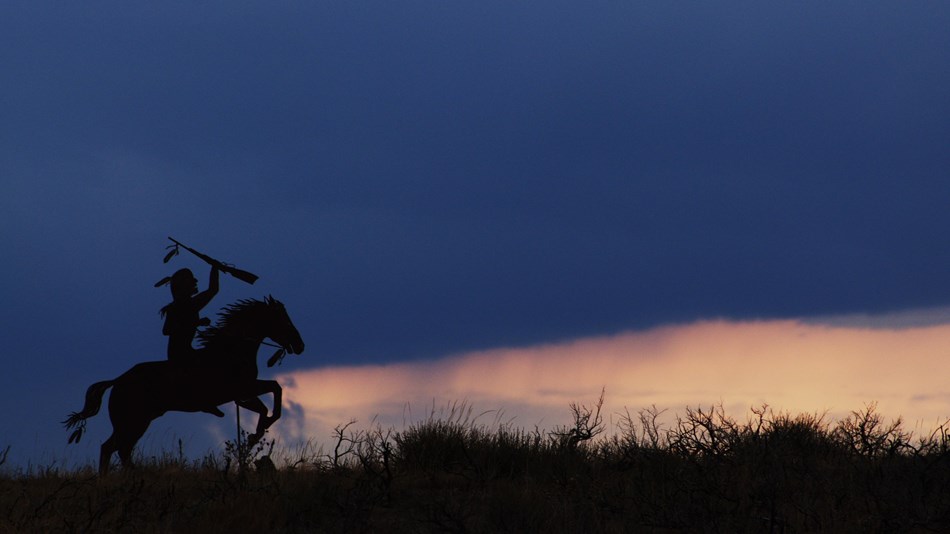 A metal silhouette of a Nez Perce on horseback with the sunset in the background.