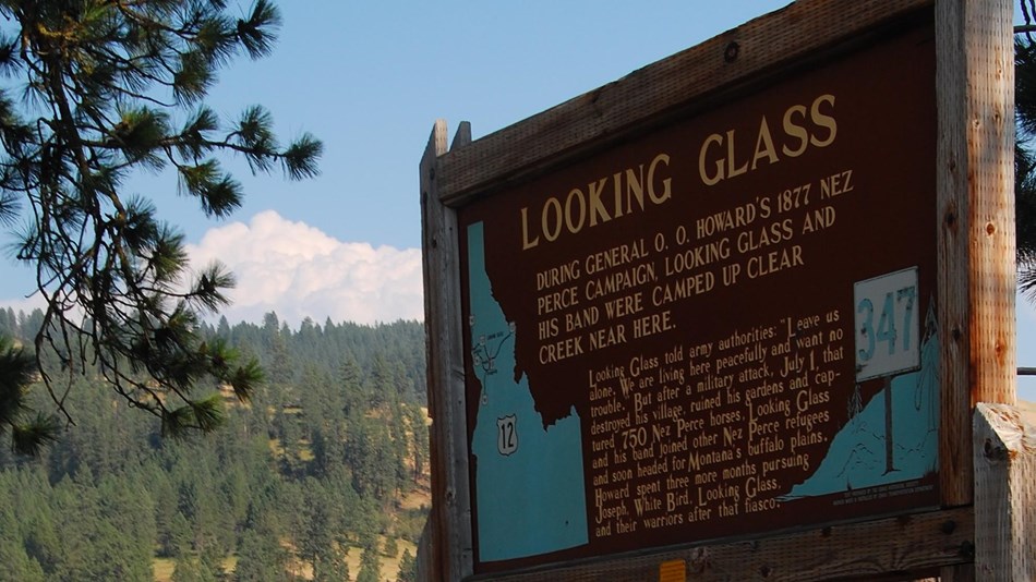 Wooden Information Sign about Looking Glass' Camp is situated near a scenic river.