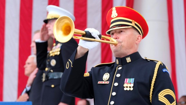 Military bugler playing in front of a large US flag