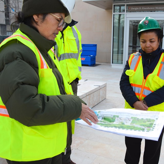 National Park Service staff in hard hats reviewing plans of a memorial