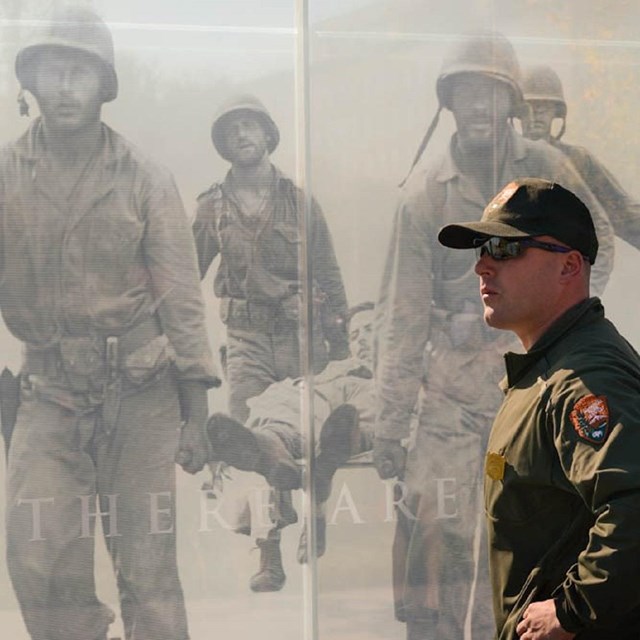 Ranger standing in front of a memorial wall with images of soliders