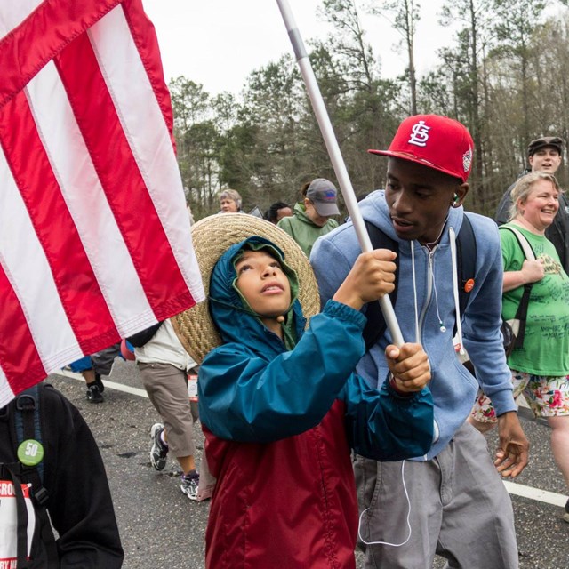 Man talking to a child holding a US flag as they march in the street 