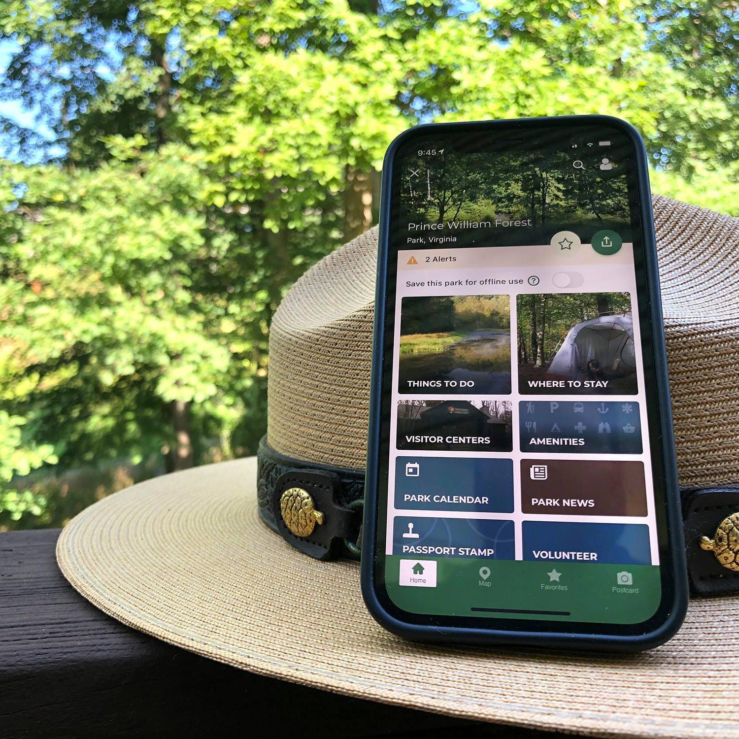 Smartphone displaying the NPS App learning on a park ranger hat