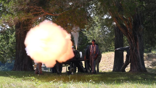 Living historians are illuminated by a cannon blast.