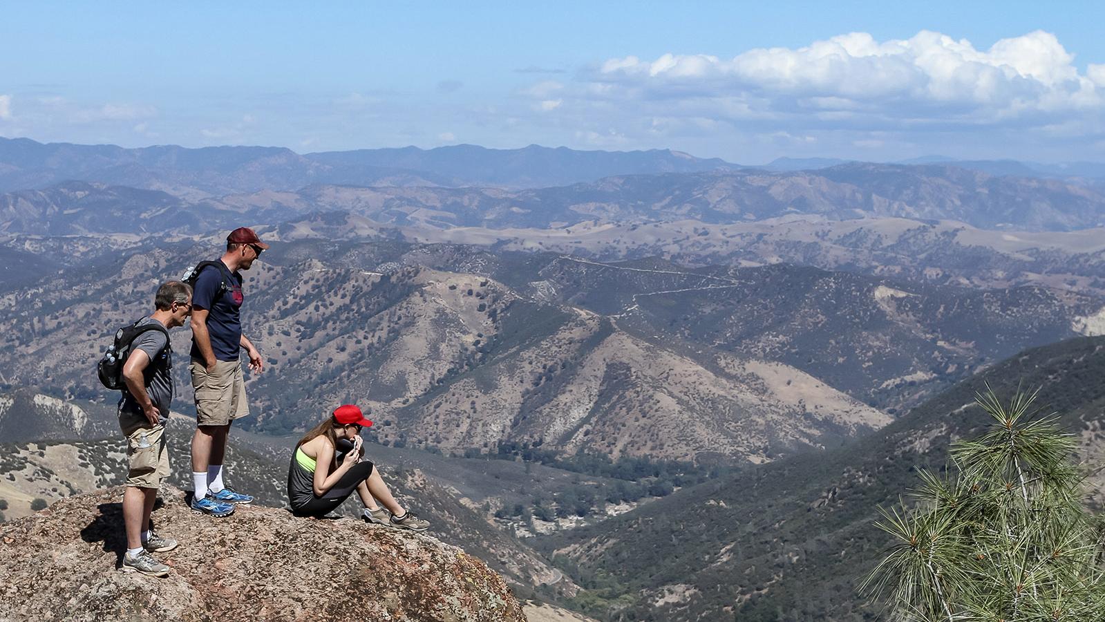 Park visitors perch on a rock beneath the open sky on a sunny day at Pinnacles National Park.