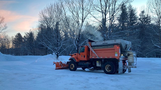 An orange snow plow truck on a snowy morning.