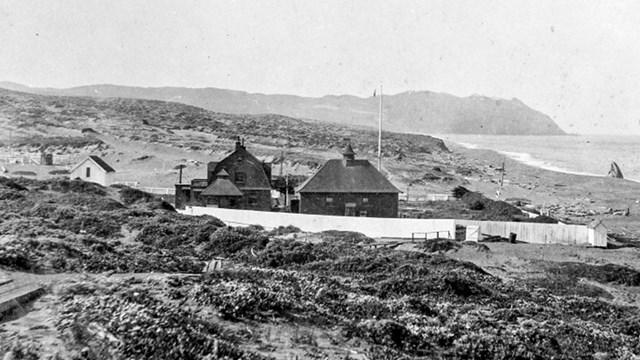 A black and white photo of several wooden structures adjacent to an ocean beach.