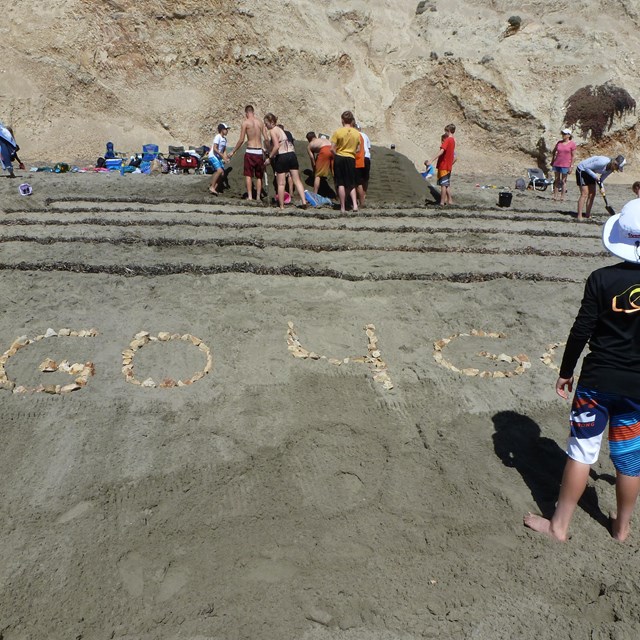 Young adults construct a sand sculpture of bleachers and a foot-race track.