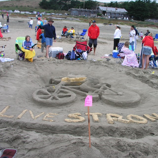A sand sculpture of a bicyclist above the words Live Strong.