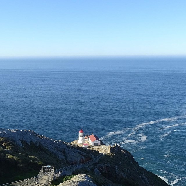 A blue ocean stretches into the distance beyond a short lighthouse sitting on a rocky headland.