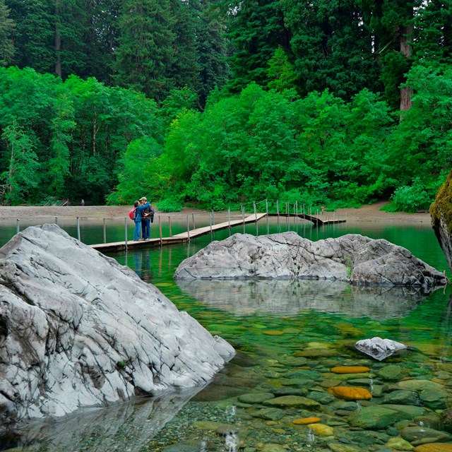 People walk across a wooden footbridge across a river