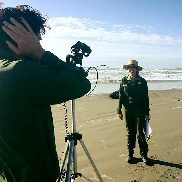 Two rangers on a beach film a video program.