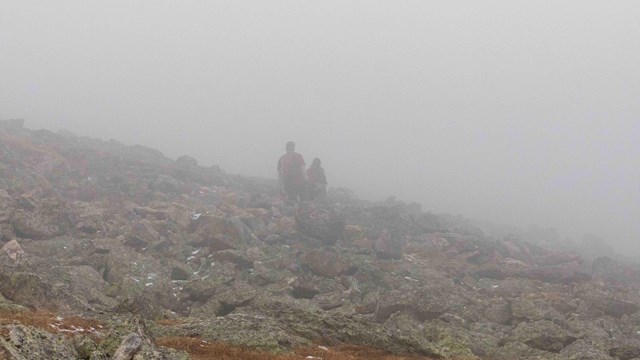 Two people are hiking in the fog with snow on the ground