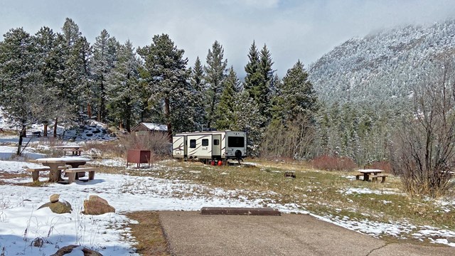 A view of a campsite in Aspenglen Campground with an RV parked. The campsite has snow on the ground