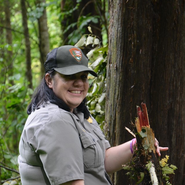 A female ranger hold up a storm damages log and grins at the camera