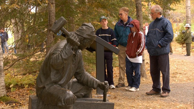 Park visitors observe a statue at Saint Croix Island IHS