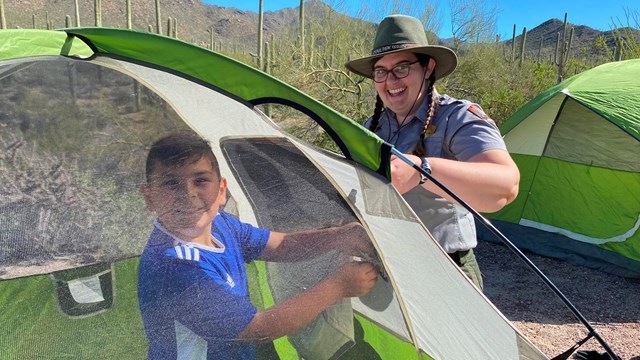 kid inside tent and ranger outside tent in desert landscape, both smiling