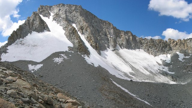 View of a steep rugged mountain with patches of ice and snow that are part of a glacier.