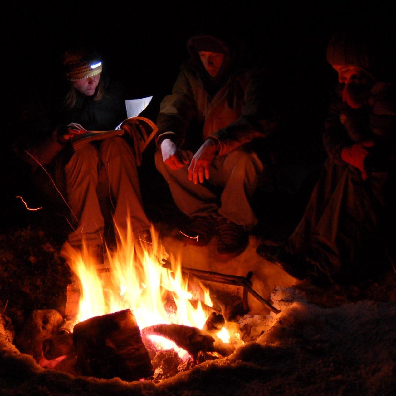 A group of campers relaxing around a fire.