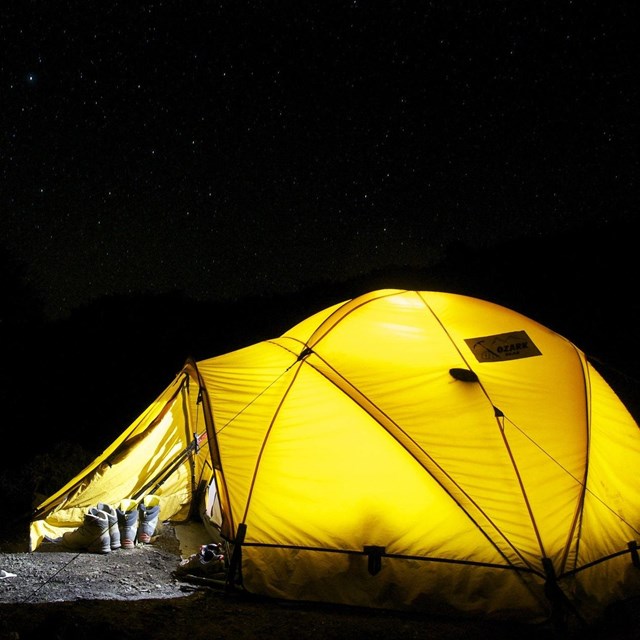 A yellow tent is set up in the middle of a dark night.