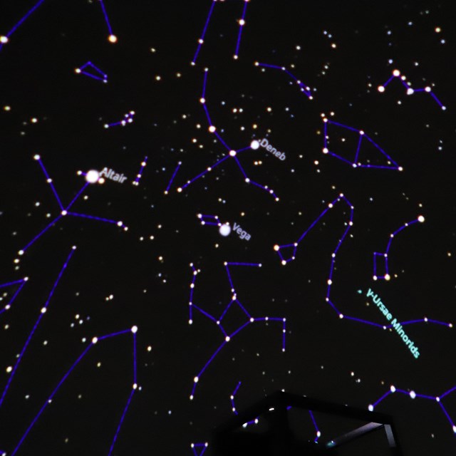 A starry night sky is projected in a dark room. Lines connect the stars to show constellations.