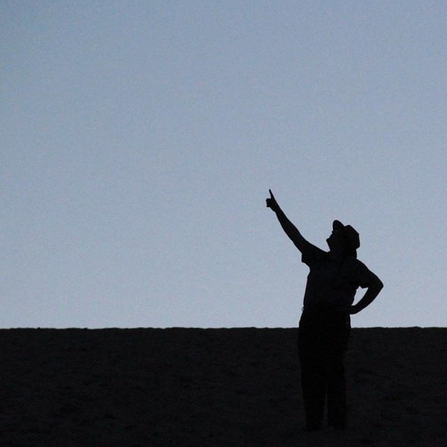 A silhouette of a ranger in uniform pointing at the sky.