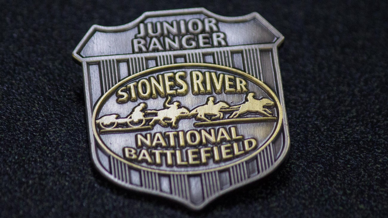 A silver badge that says "Junior Ranger Stones River National Battlefield"