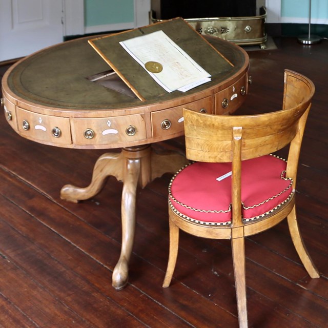 A photograph of a round desk in the center of a room with a chair in front of it. 