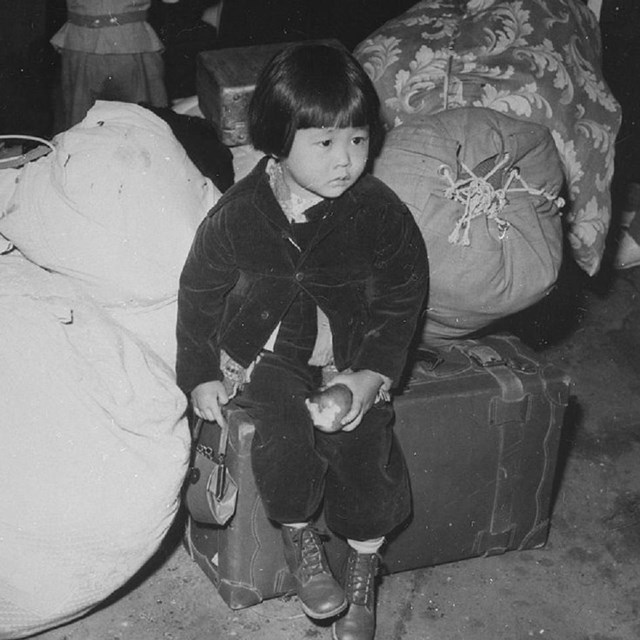 Small child sitting on pile of luggage. 