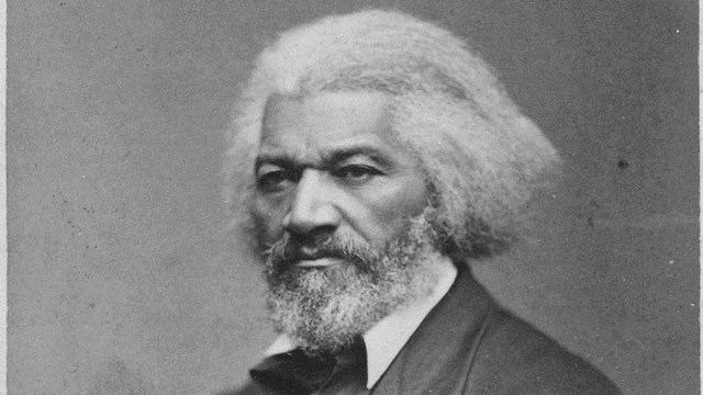 An older Frederick Douglass with white hair, sitting. 