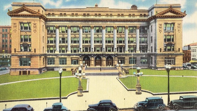 Color postcard of courthouse. Six stories, pediments, columns, arched entrance, many windows.