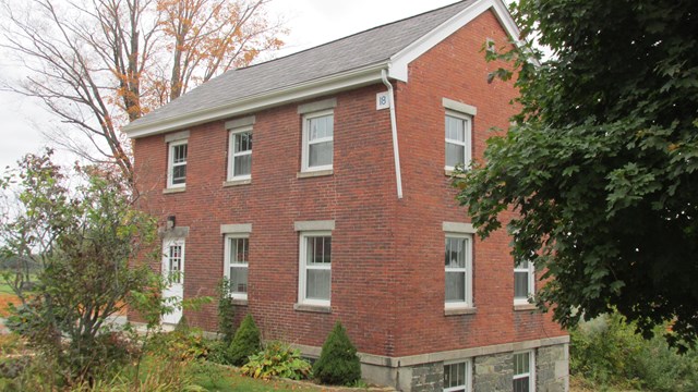 two-story brick building surrounded by trees in early fall