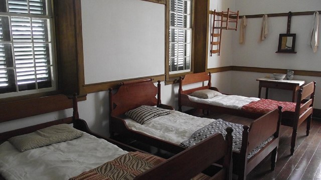 shaker bed room with three beds, wooden bed frames, and simple quilts