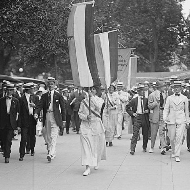 Black and white photo of women carrying suffrage banners and marching. Library of Congress. 