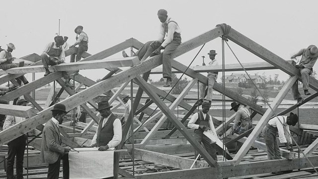 Black and white image showing a group of students constructing a wooden framework for a building.