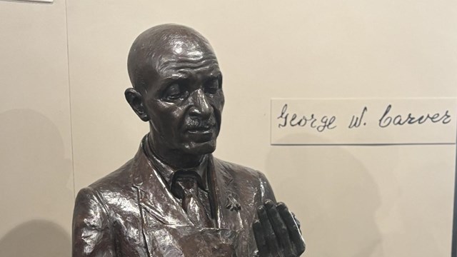 Bronze bust of George Washington Carver displayed on a gray pedestal.
