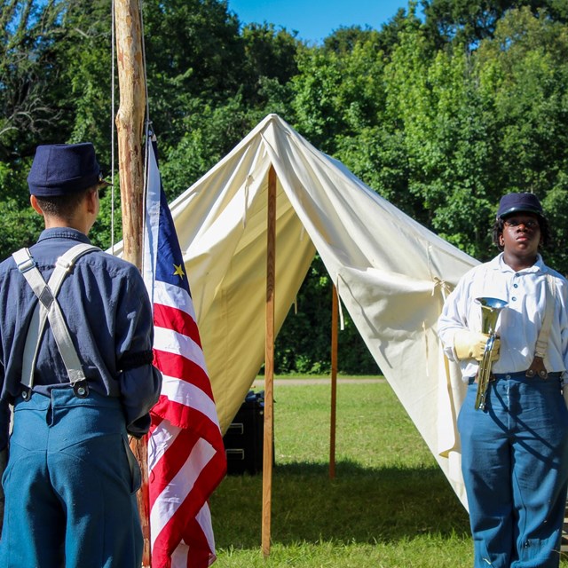 Men dressed in civil war period clothing lower a flag