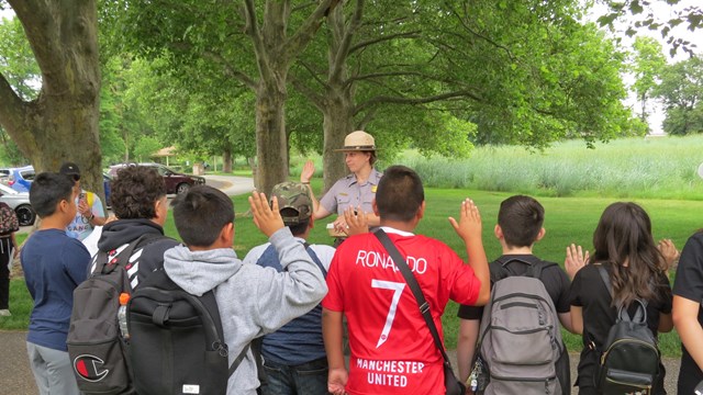 A ranger stands with their right hand raised in front of a group of 4th grade students