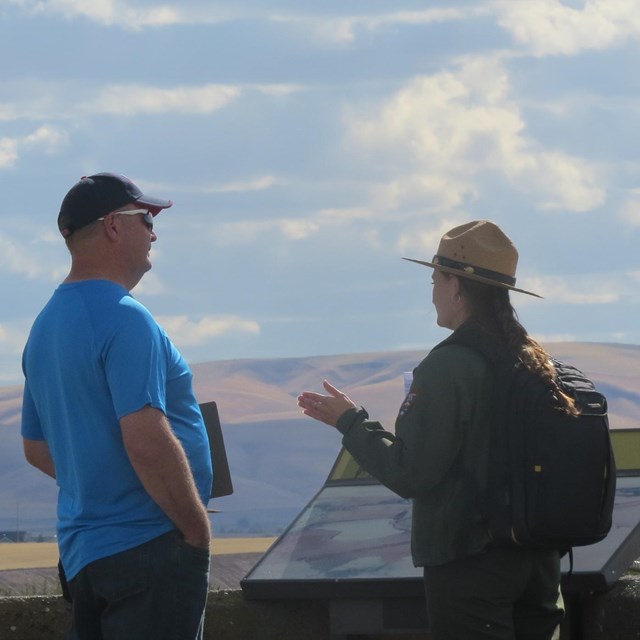 A ranger and visitor talking while overlooking a mountain range in the distance