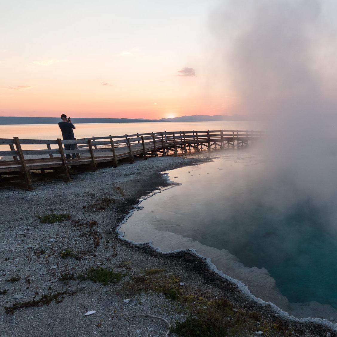 A person walks on a boardwalk near a hot spring at sunrise.