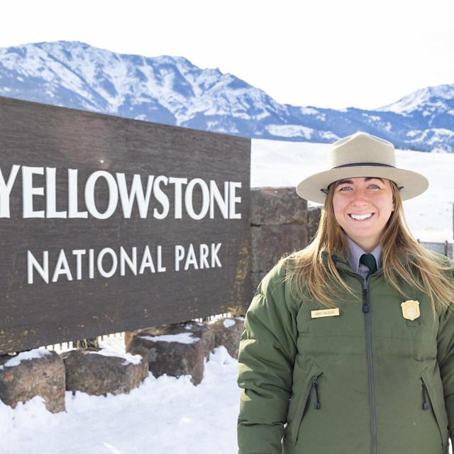 a park ranger in uniform smiling in front of a park sign