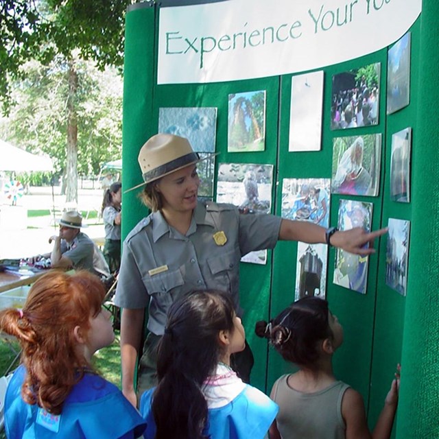 Park Ranger pointing to pictures with kids at a community event.