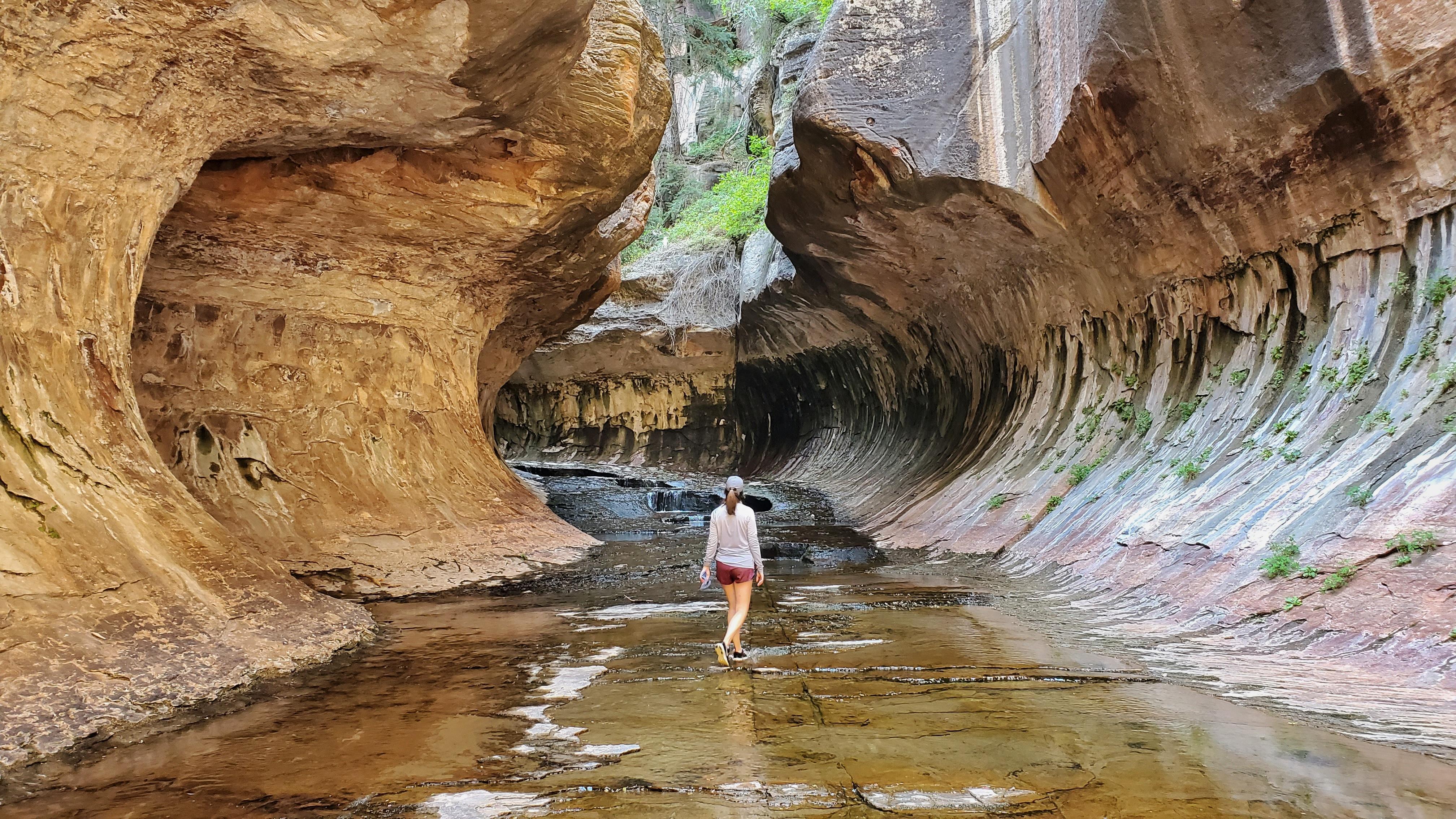 Person walking in water between curved rocks that look like a tunnel