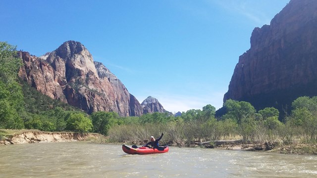 Visitors float down a river between towering canyon walls in an inflatable kayak.