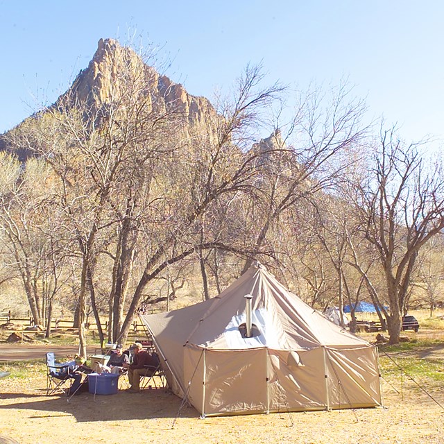 Canvas tent with people having a picnic. Sandstone mountain called The Watchman in background.