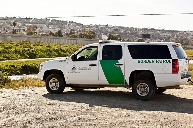 white and green suv with border patrol markings is parked above a wall