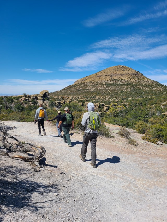 hikers on trail with backpacks and mountain in distance