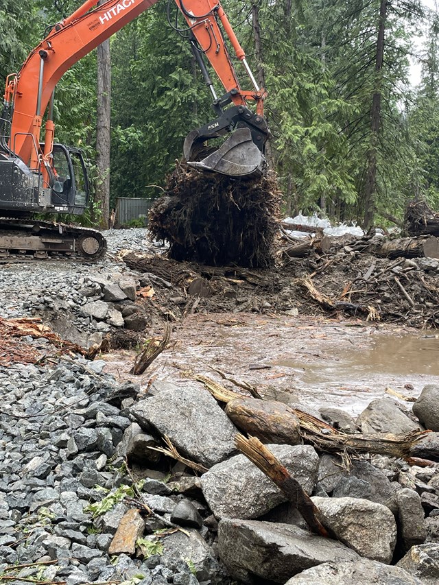 an excavator works on a large dirt ball between a gravel bed and mud muddle
